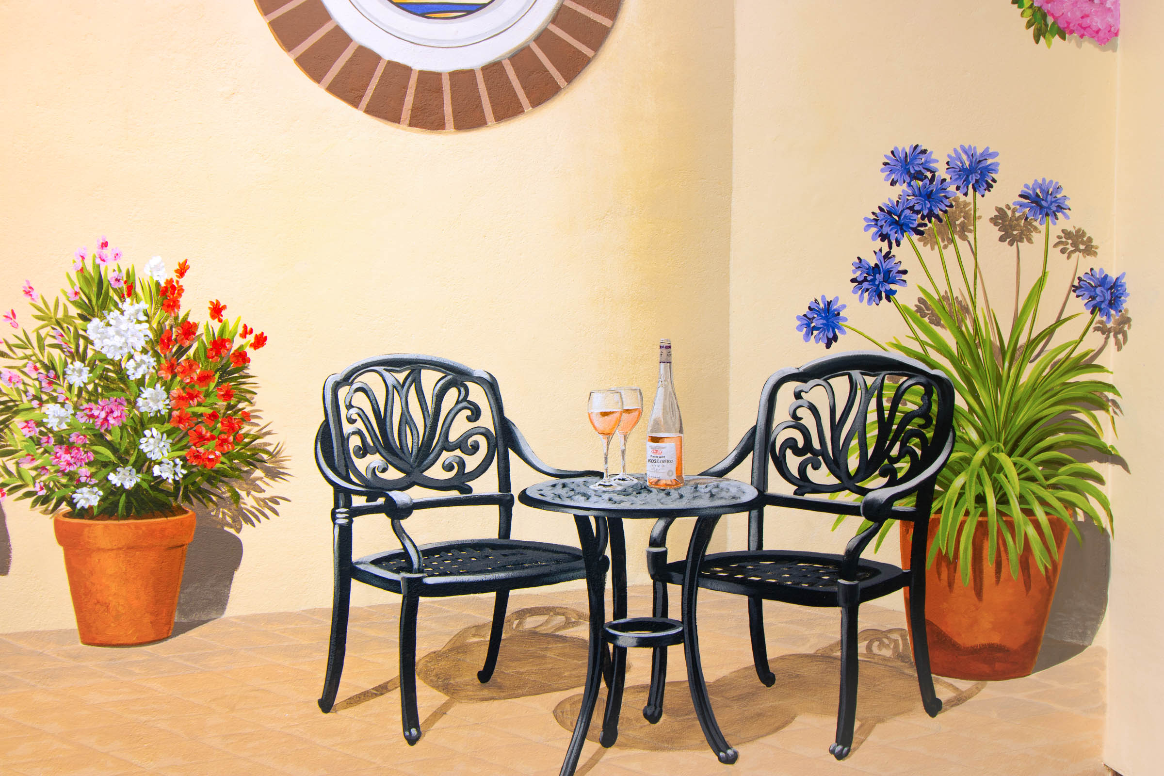 Patio trompe l'oeil with inviting table and chairs, flanked by splendid oleander and agapanthus