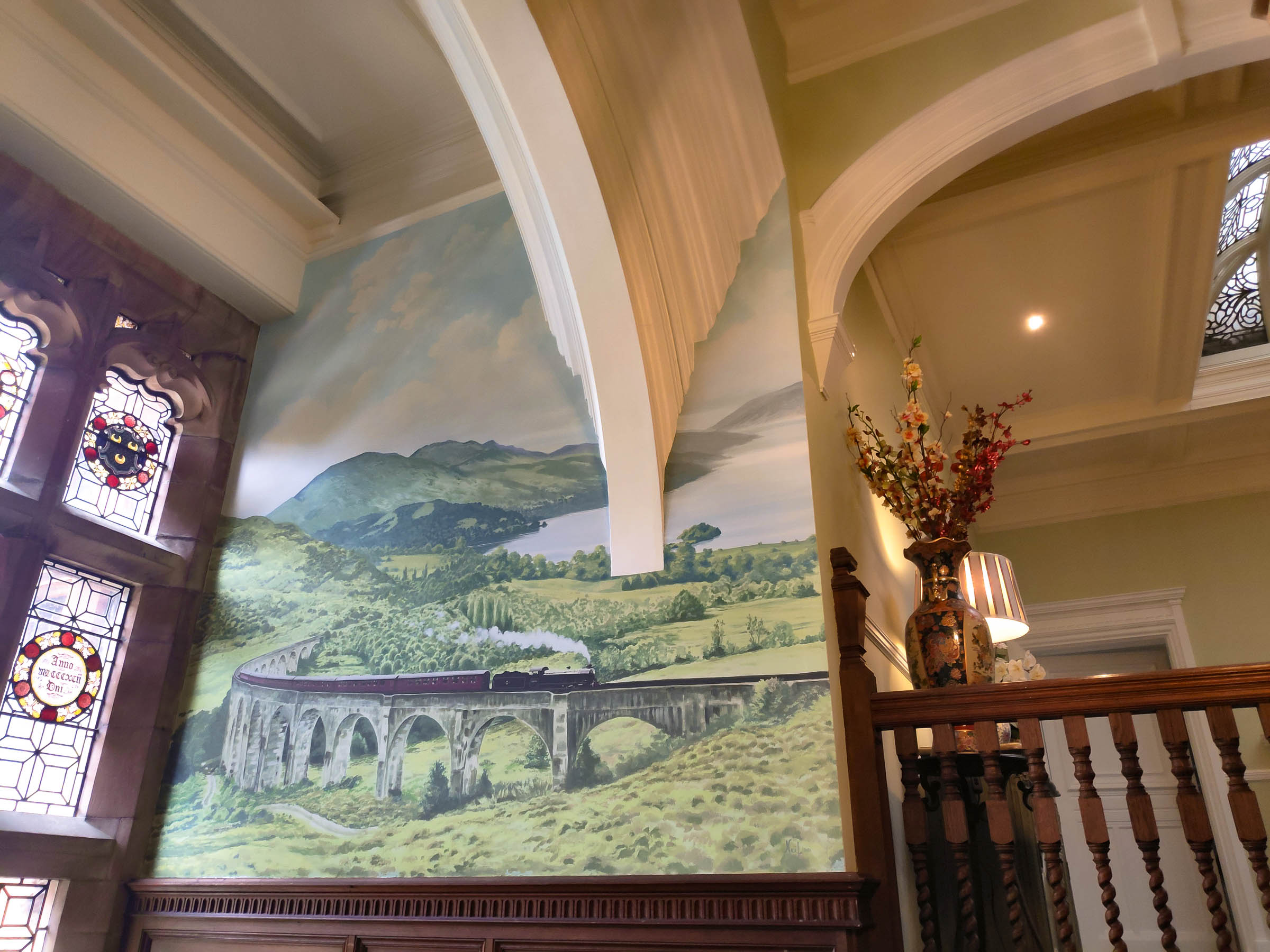 Mural beside a grand stairway and window.