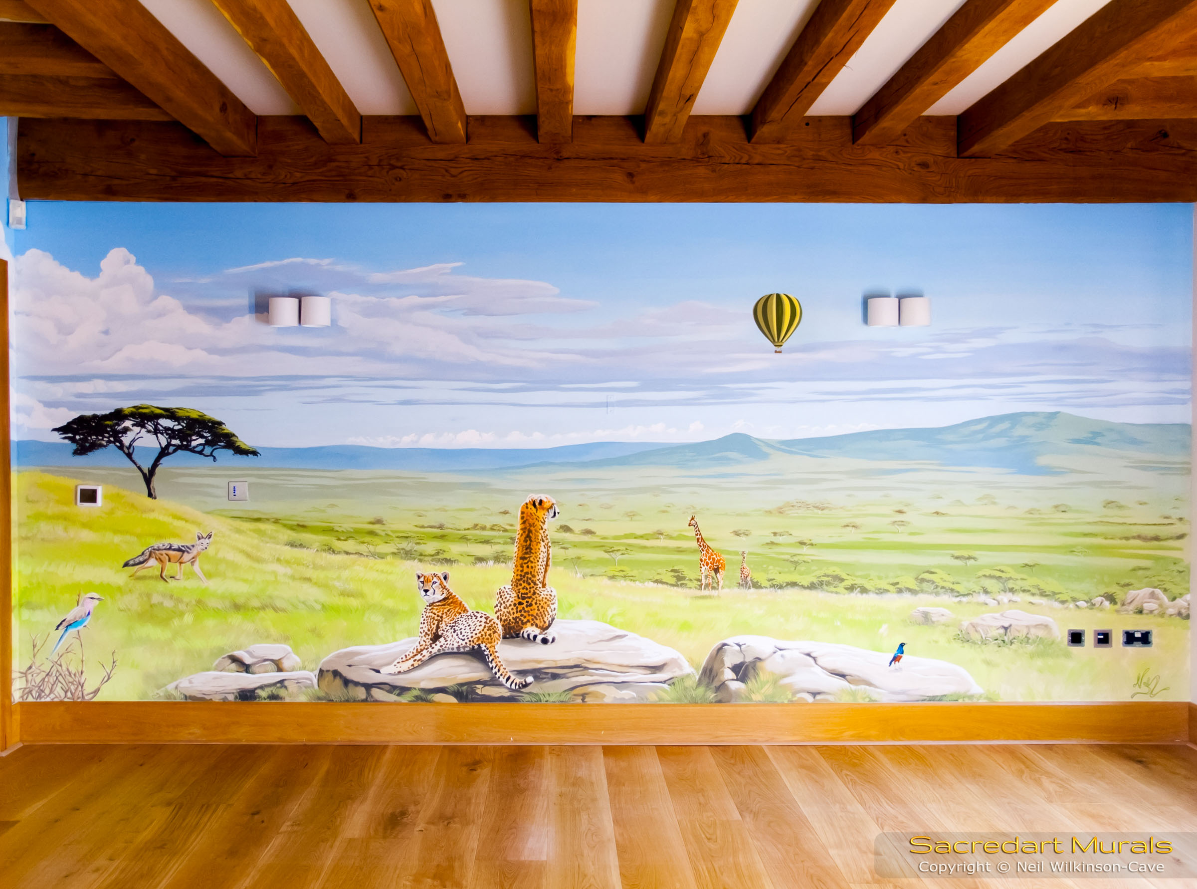 Safari Mural - Showing the right wall with a view looking down from up a hill, towards the Serengeti plains below, with cheetahs sitting on a rock, a jackal, giraffes, some birds and a hot air balloon